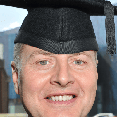 A head shot of Mike Everett wearing a mortarboard on graduation day stood outside the Wycombe Swan Theatre